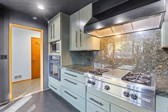 kitchen featuring appliances with stainless steel finishes, gray cabinetry, decorative backsplash, dark stone counters, and wall chimney exhaust hood