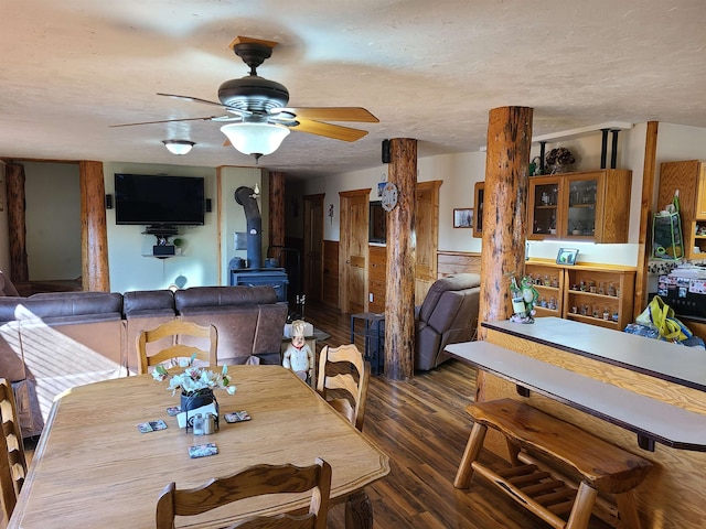 dining area with a textured ceiling, dark hardwood / wood-style floors, a wood stove, and ceiling fan