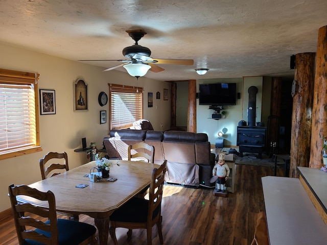 dining room featuring dark wood-type flooring, a textured ceiling, a wood stove, and ceiling fan