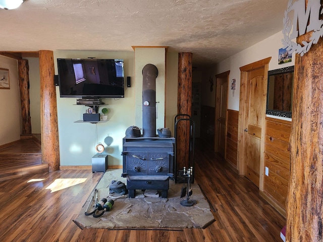 living room with wood walls, a textured ceiling, a wood stove, and dark hardwood / wood-style flooring