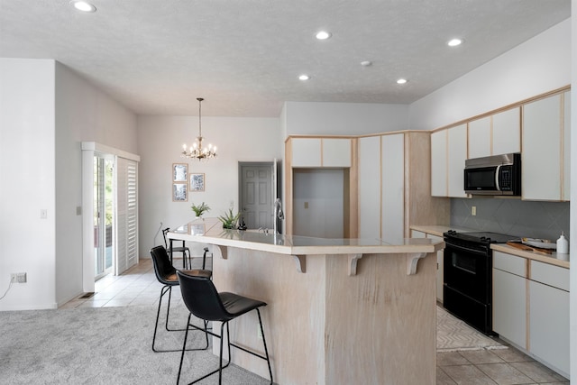 kitchen featuring white cabinets, light tile patterned floors, electric range, and an island with sink