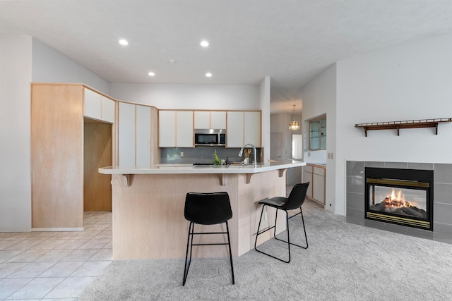 kitchen featuring sink, a kitchen bar, a tile fireplace, light tile patterned floors, and a center island with sink