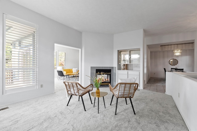 sitting room featuring a wealth of natural light, a tiled fireplace, and light colored carpet