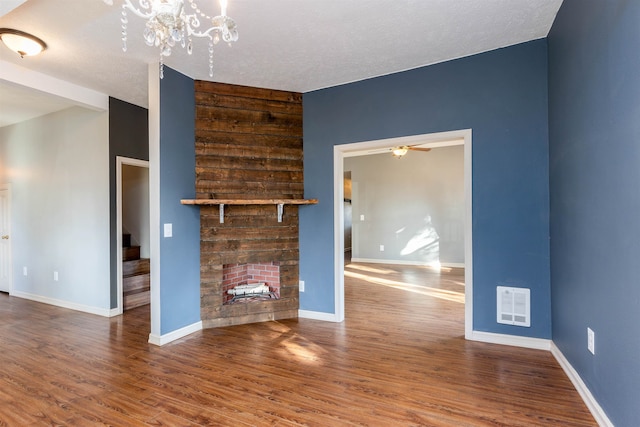 unfurnished living room with hardwood / wood-style floors, a fireplace, a textured ceiling, and ceiling fan with notable chandelier