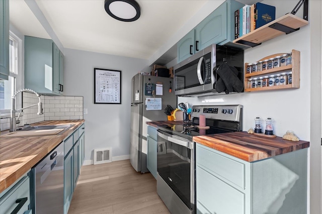 kitchen featuring light wood-type flooring, tasteful backsplash, stainless steel appliances, sink, and butcher block countertops