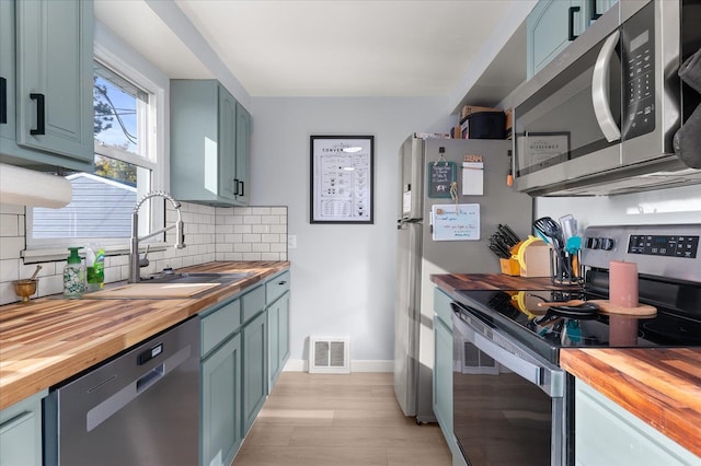 kitchen featuring tasteful backsplash, butcher block countertops, stainless steel appliances, and sink