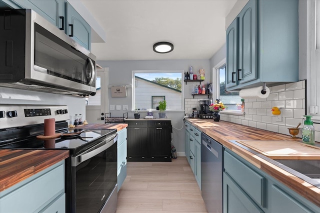 kitchen featuring decorative backsplash, blue cabinetry, stainless steel appliances, and butcher block counters