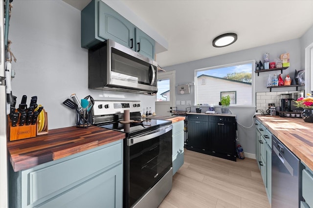 kitchen featuring light wood-type flooring, open shelves, tasteful backsplash, appliances with stainless steel finishes, and butcher block counters