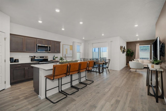 kitchen featuring dark brown cabinets, a kitchen island, appliances with stainless steel finishes, a kitchen breakfast bar, and light hardwood / wood-style flooring