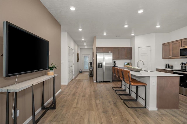 kitchen with wood-type flooring, a center island with sink, sink, a kitchen bar, and appliances with stainless steel finishes