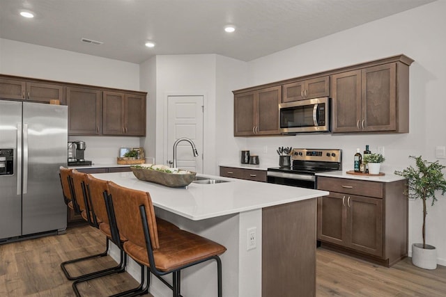 kitchen with a center island with sink, sink, stainless steel appliances, and wood-type flooring