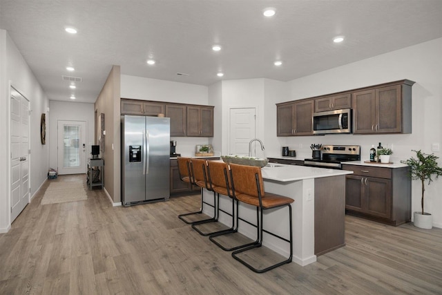 kitchen with appliances with stainless steel finishes, a breakfast bar area, light wood-type flooring, and a center island with sink