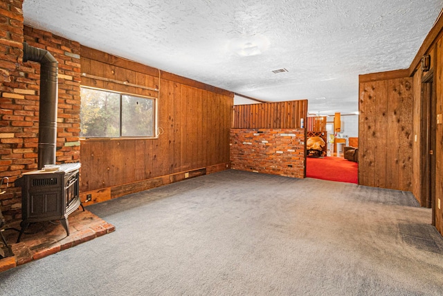 living room with a wood stove, a textured ceiling, wooden walls, and carpet flooring