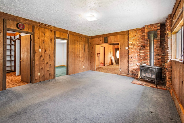 unfurnished living room with wooden walls, a textured ceiling, carpet floors, and a wood stove