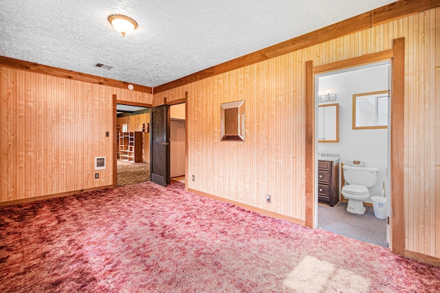 unfurnished bedroom with heating unit, a textured ceiling, carpet flooring, connected bathroom, and wood walls