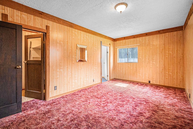 carpeted spare room with a textured ceiling and wooden walls