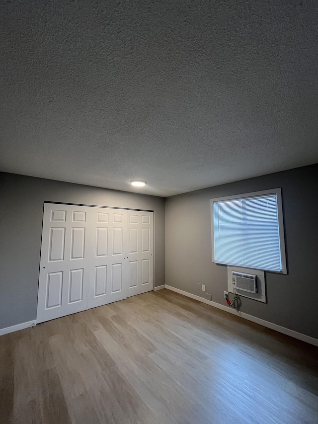 unfurnished bedroom with a wall mounted air conditioner, a textured ceiling, and light wood-type flooring