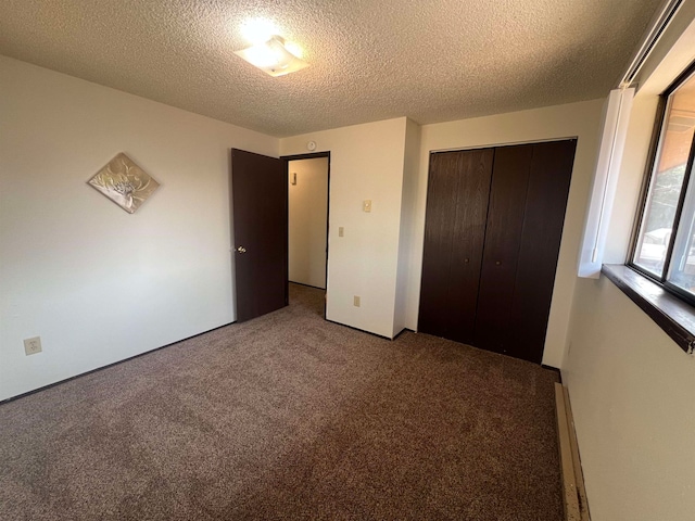 unfurnished bedroom featuring a baseboard heating unit, a textured ceiling, a closet, and carpet floors