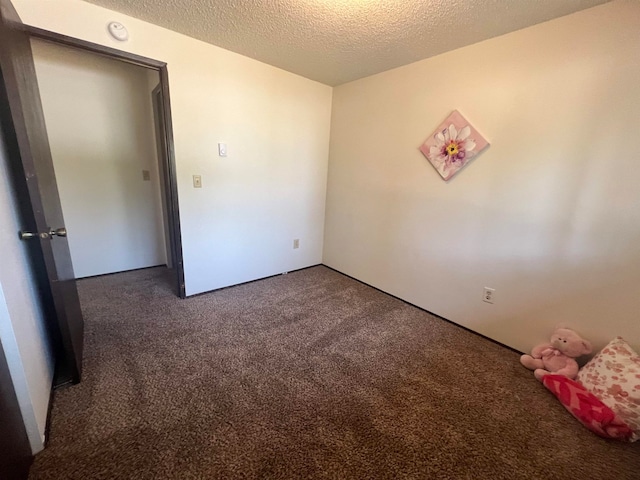 empty room with a textured ceiling and dark colored carpet