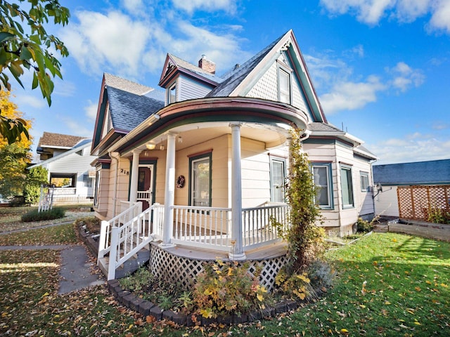 victorian-style house with a porch, a front yard, roof with shingles, and a chimney