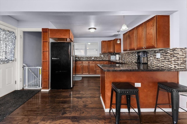 kitchen featuring kitchen peninsula, dark hardwood / wood-style flooring, black fridge, a kitchen bar, and pendant lighting