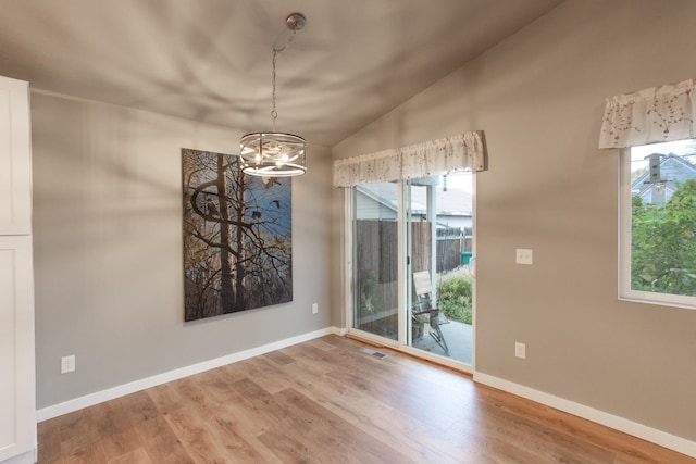 unfurnished dining area featuring a notable chandelier, hardwood / wood-style flooring, and lofted ceiling