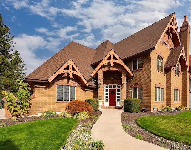 view of front of house with a front yard, brick siding, and roof with shingles