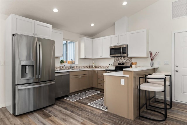 kitchen with kitchen peninsula, lofted ceiling, a breakfast bar area, appliances with stainless steel finishes, and white cabinetry