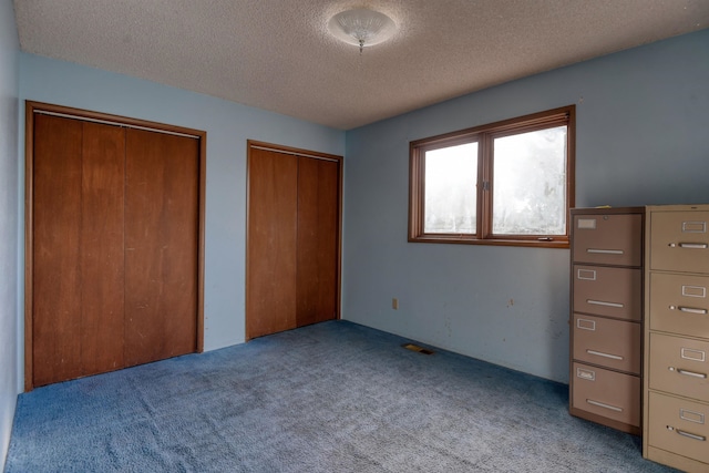 unfurnished bedroom with multiple closets, a textured ceiling, and light colored carpet