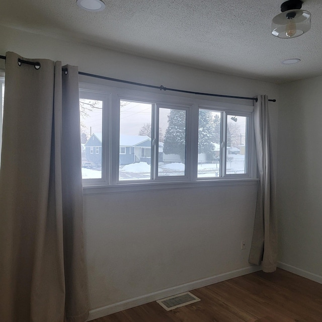 spare room featuring dark wood-style flooring, visible vents, a textured ceiling, and baseboards