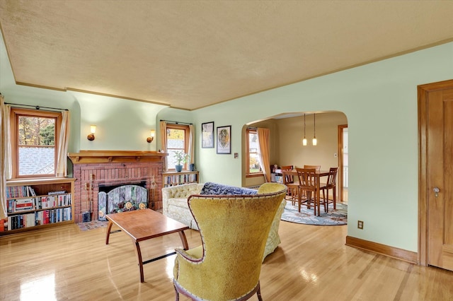 living room featuring light wood-type flooring, a textured ceiling, a wealth of natural light, and a brick fireplace