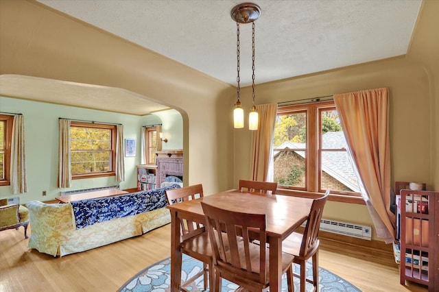 dining room featuring light hardwood / wood-style flooring, a textured ceiling, a baseboard radiator, and a brick fireplace