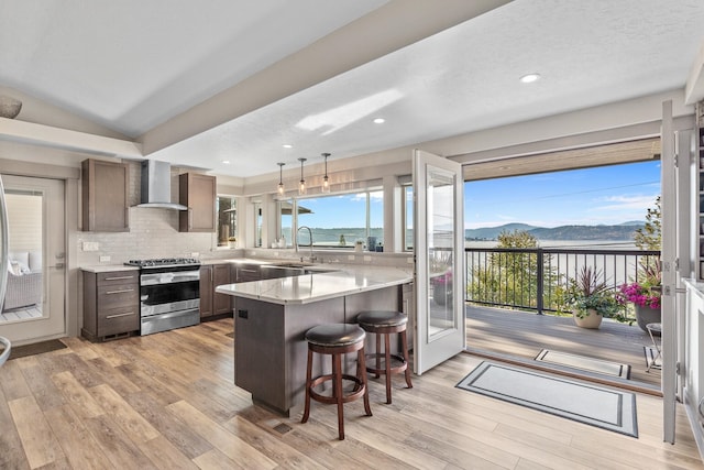 kitchen with wall chimney range hood, kitchen peninsula, decorative light fixtures, a mountain view, and stainless steel gas range