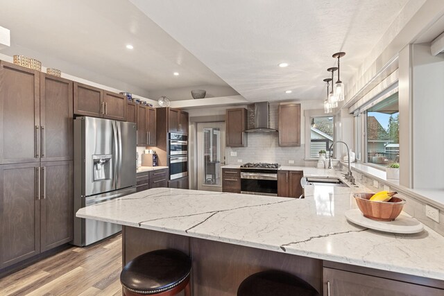 kitchen featuring appliances with stainless steel finishes, pendant lighting, light hardwood / wood-style floors, wall chimney exhaust hood, and sink