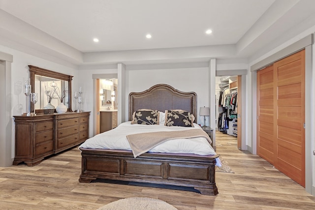 bedroom with a closet, ensuite bath, and light wood-type flooring