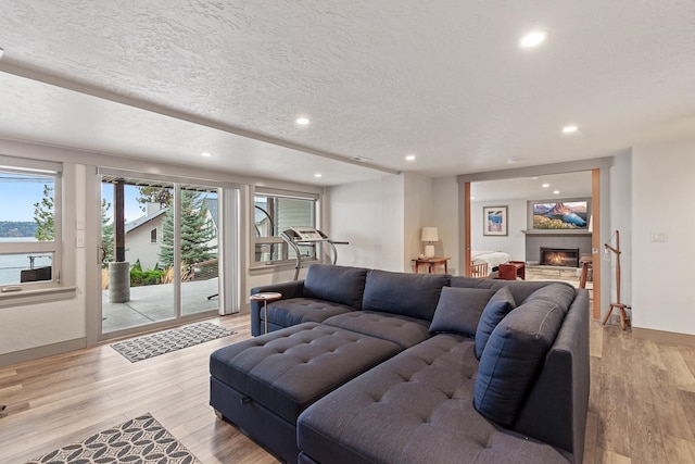 living room with light hardwood / wood-style floors, a textured ceiling, a tiled fireplace, and a wealth of natural light