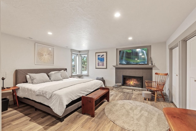 bedroom with a textured ceiling, light hardwood / wood-style flooring, and a fireplace