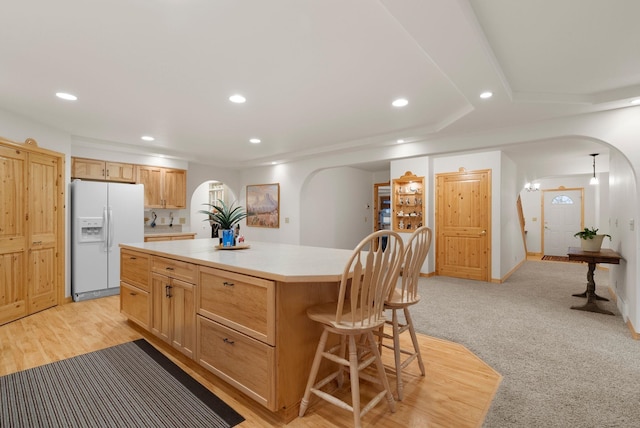 kitchen featuring light carpet, light brown cabinetry, white refrigerator with ice dispenser, and a kitchen island