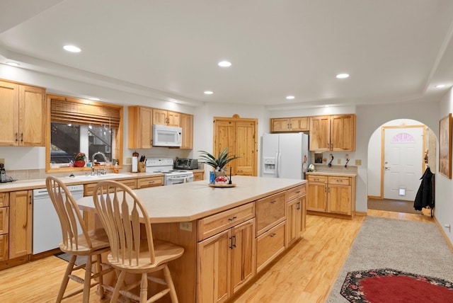 kitchen featuring white appliances, sink, a kitchen bar, a center island, and light hardwood / wood-style floors