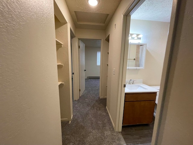 hall featuring a baseboard radiator, sink, dark carpet, and a textured ceiling