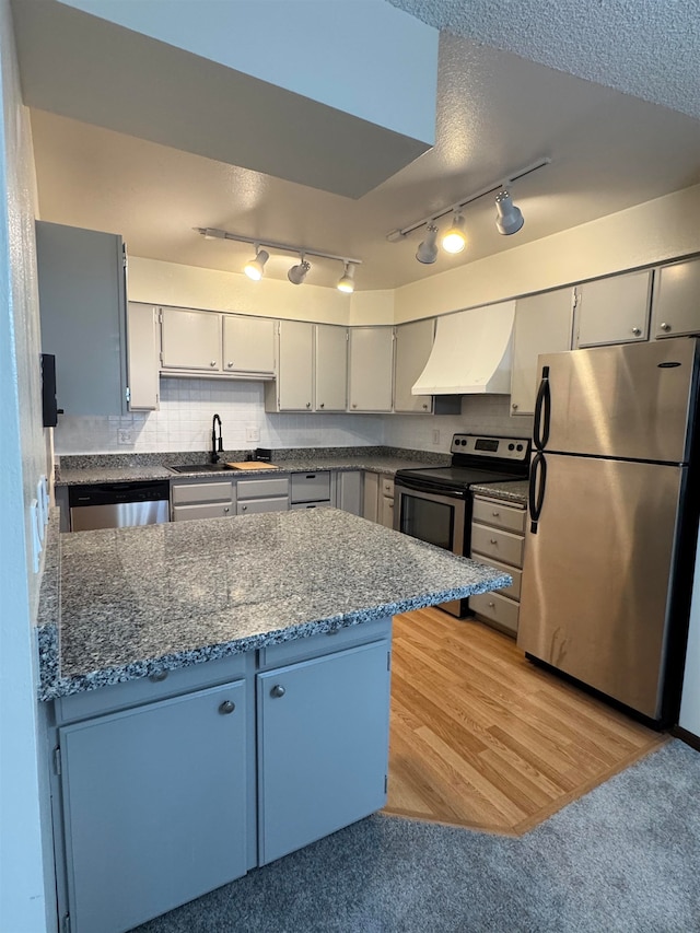 kitchen featuring dark stone counters, backsplash, appliances with stainless steel finishes, exhaust hood, and light hardwood / wood-style flooring