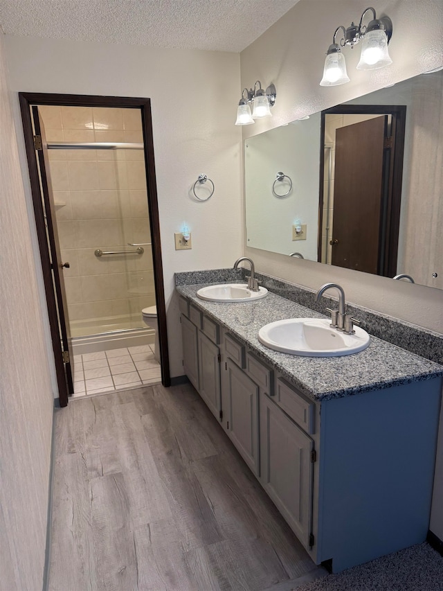 bathroom with wood-type flooring, a tile shower, vanity, a textured ceiling, and toilet