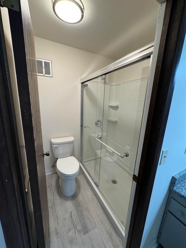 bathroom with toilet, vanity, wood-type flooring, and a shower with door