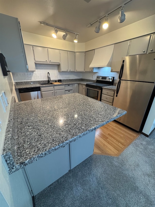 kitchen with custom range hood, stainless steel appliances, kitchen peninsula, and sink