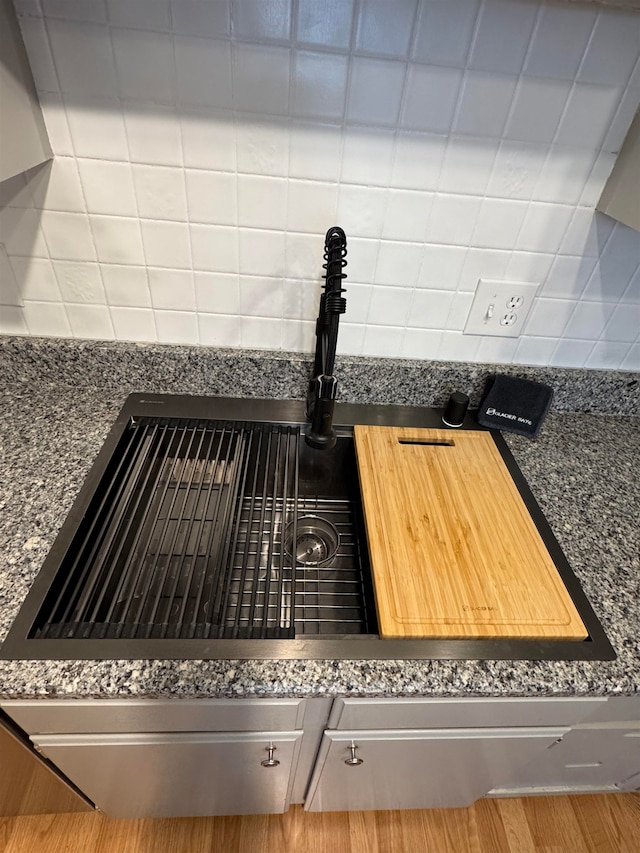 details featuring wood-type flooring, dark stone countertops, and backsplash