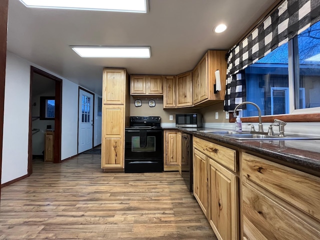 kitchen with dark stone countertops, sink, black appliances, and light wood-type flooring