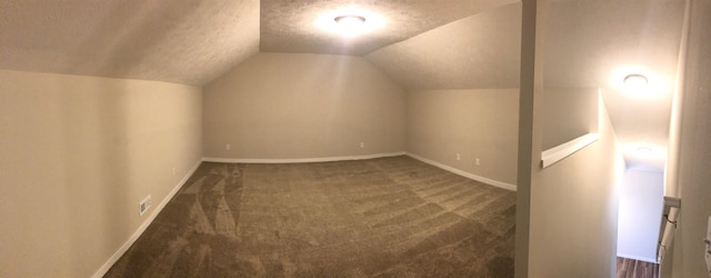 additional living space with lofted ceiling, a textured ceiling, and dark colored carpet