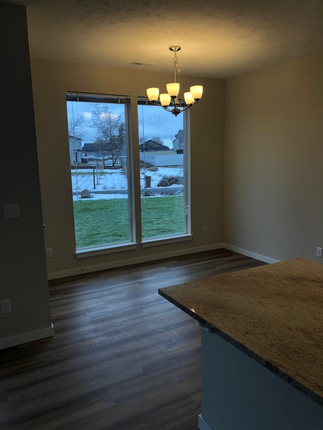 unfurnished dining area with a chandelier, a textured ceiling, and dark hardwood / wood-style flooring