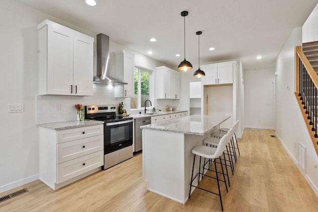 kitchen featuring stainless steel appliances, white cabinetry, wall chimney range hood, light hardwood / wood-style floors, and a center island