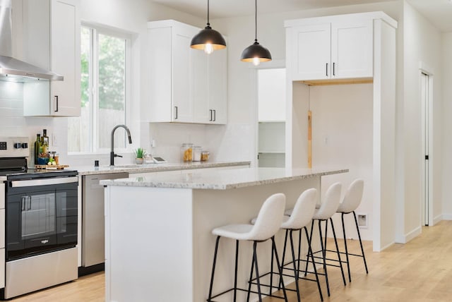 kitchen with white cabinets, wall chimney range hood, stainless steel appliances, and a center island